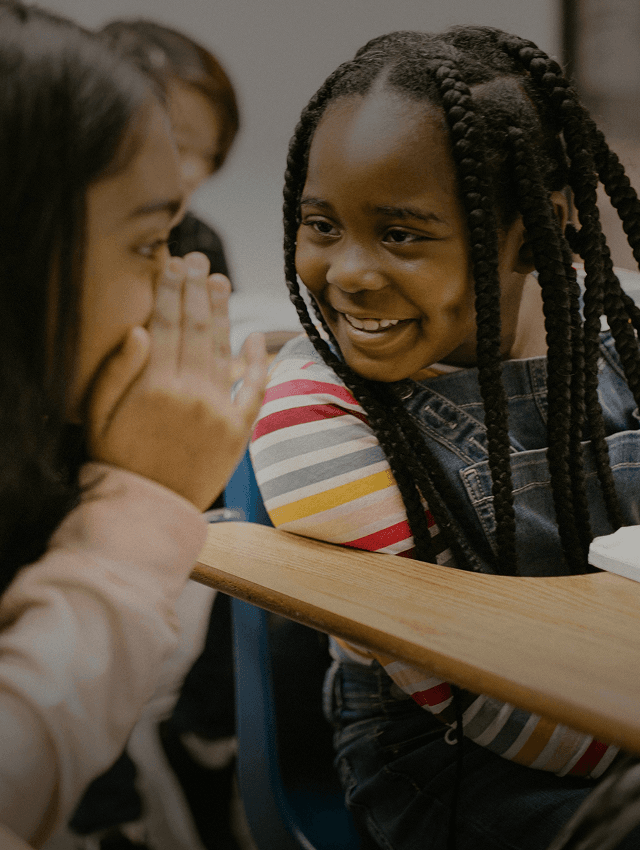 Alunos sorridentes sussurram uns aos outros enquanto aprendem um novo idioma na escola.